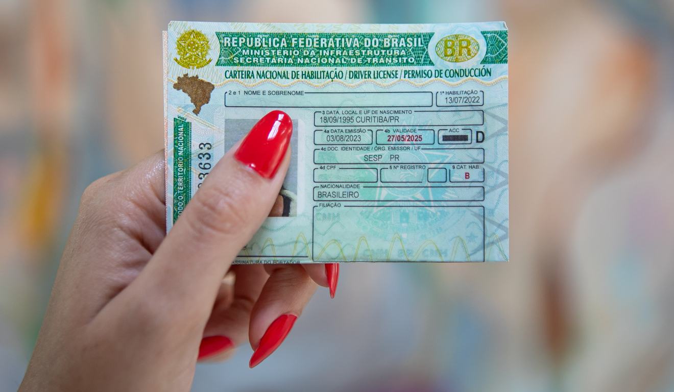 Mão feminina mostra uma carteira nacional de habilitação, CNH