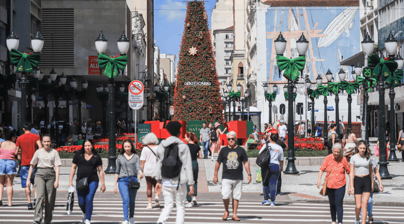 pessoas caminhando na rua xv de novembro, no centro de curitiba, com decoração de natal ao fundo e céu azul