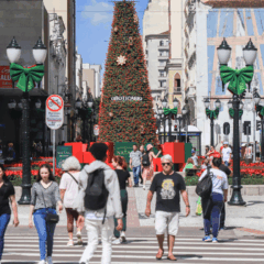 pessoas caminhando na rua xv de novembro, no centro de curitiba, com decoração de natal ao fundo e céu azul
