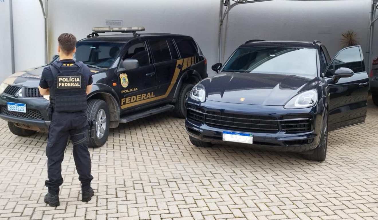 Policial federal de costas ao lado de carro de alto valor apreendido em operação