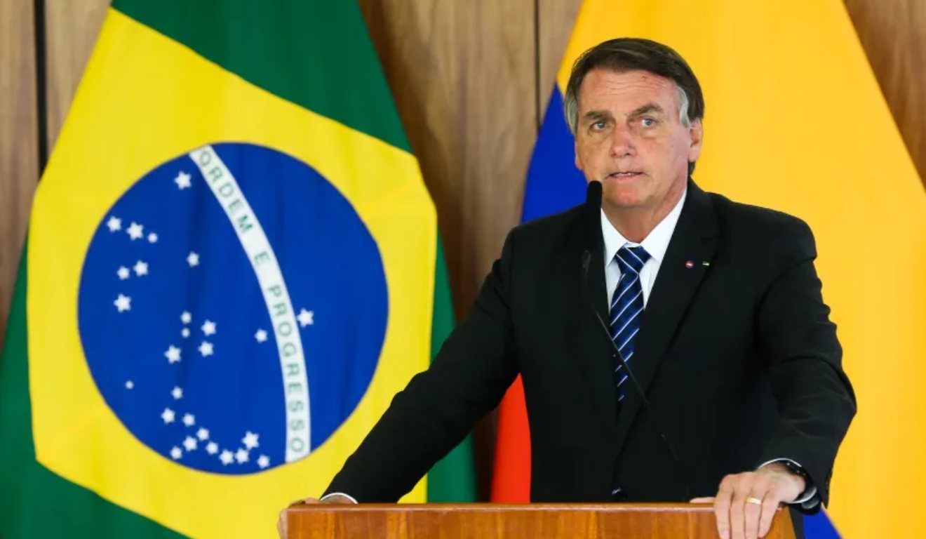 Jair Bolsonaro em palanque com bandeira do Brasil no fundo