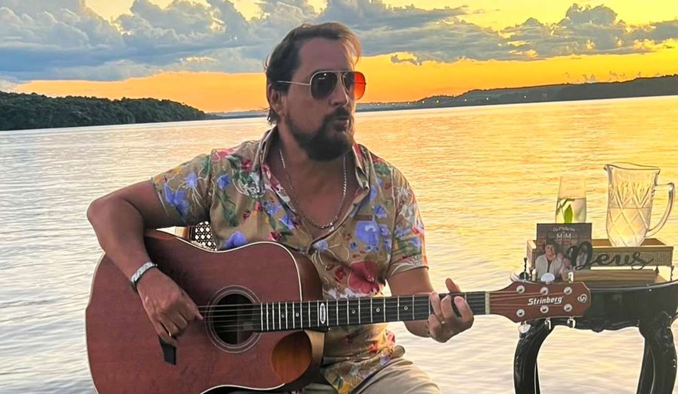 Mauri com um violão na beira de um rio