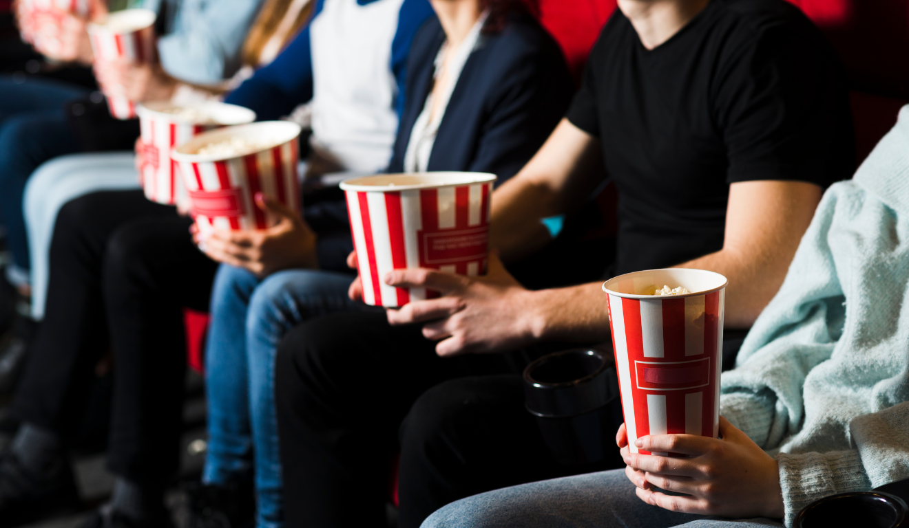 Na imagem ilustrativa, vemos pessoas sentadas em cadeiras de cinema, com pacotes de pipoca, representando eventos culturais que ampliarão o acesso à meia-entrada no Paraná.