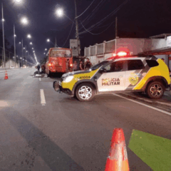 Na imagem, vemos o ônibus e a moto envolvidas no acidente. No primeiro plano, uma viatura da Polícia Militar; o motociclista bateu no ônibus, caiu e foi atropelado por um caminhão, em Piraquara.