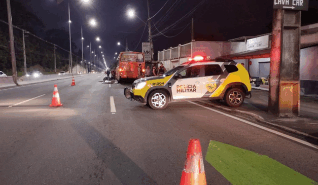 Na imagem, vemos o ônibus e a moto envolvidas no acidente. No primeiro plano, uma viatura da Polícia Militar; o motociclista bateu no ônibus, caiu e foi atropelado por um caminhão, em Piraquara.