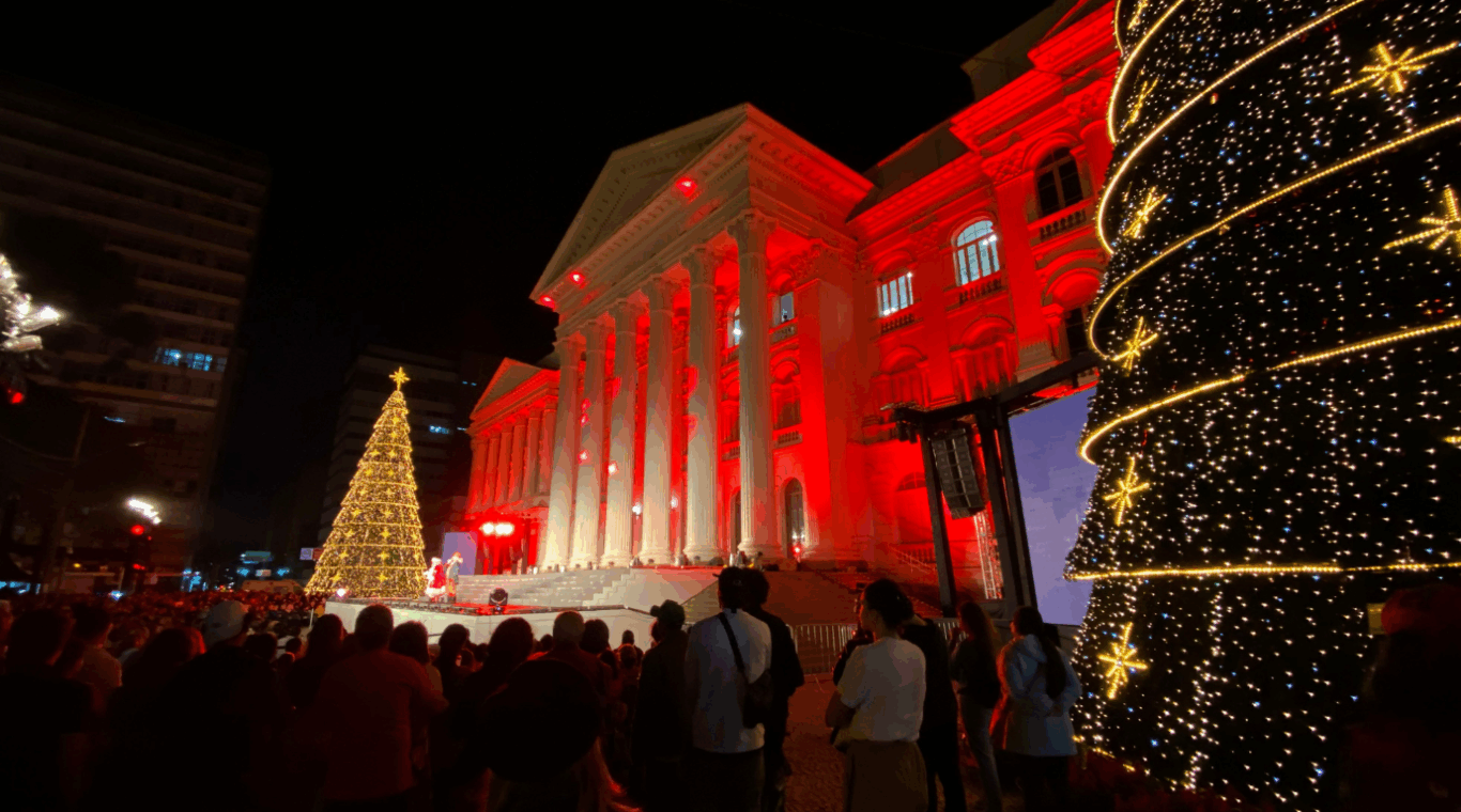 Praça Santos Andrade, em Curitiba, iluminada e com árvores de Natal acesas durante a noite