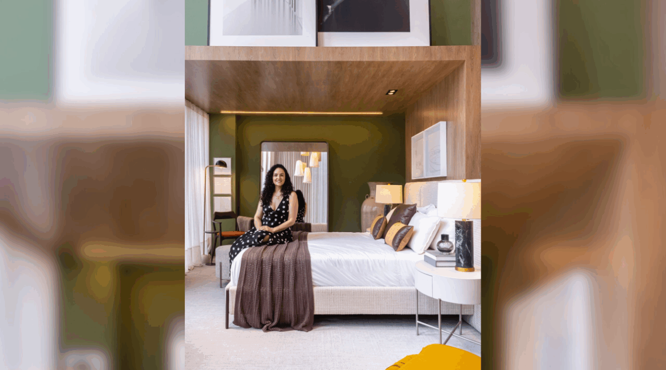 Vivian Lazzaroto sentada na cama na Vitrine Villa Batel com quarto arrumado