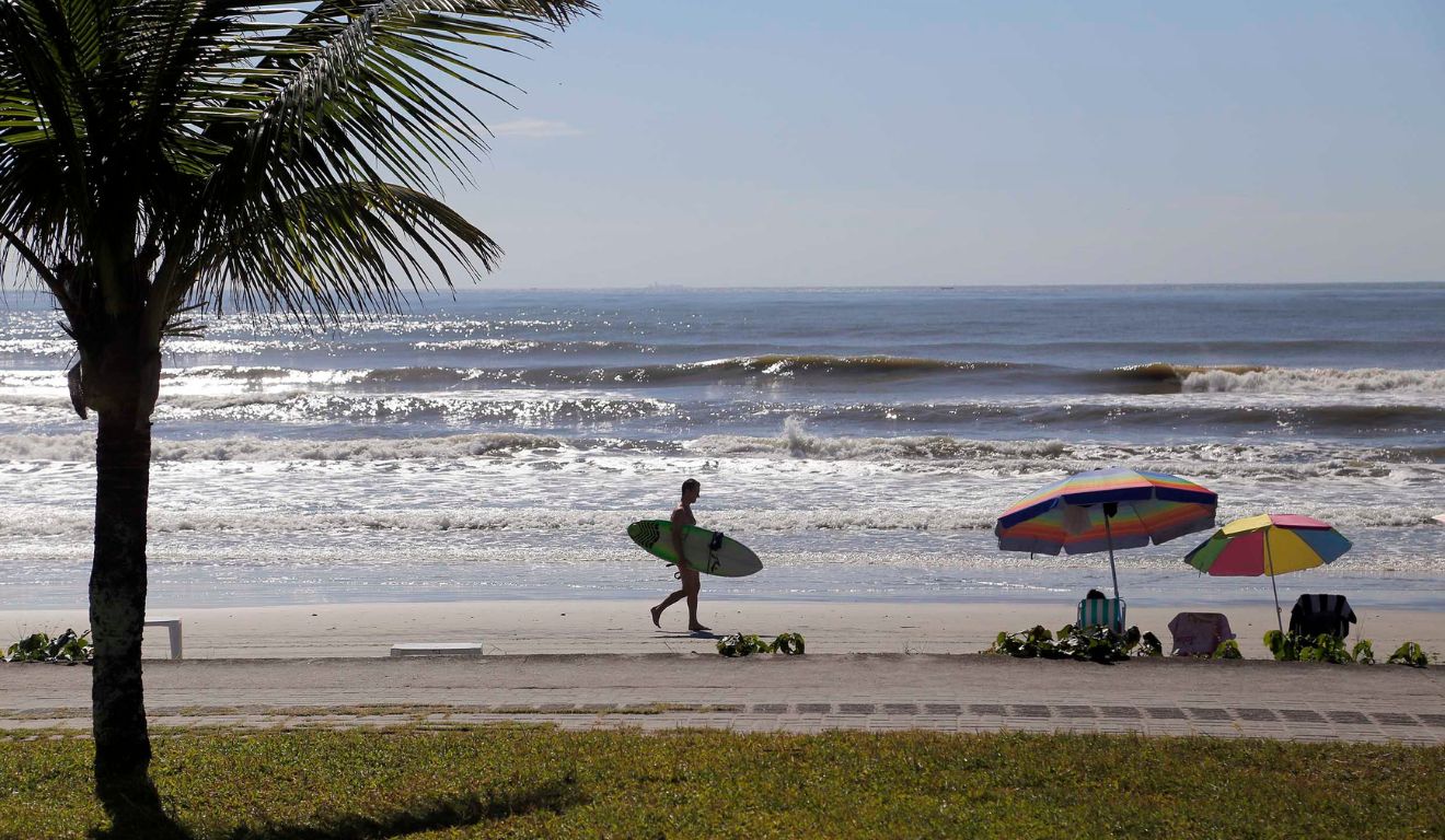 surfista andando na praia para ilustrar volta do calor no paraná