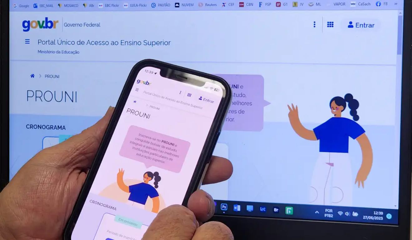 Candidato com celular nas mãos em frente a um computador para fazer a inscrição no Prouni