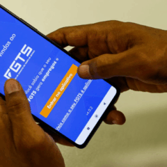 M&atilde;os de uma pessoa negra segurando um celular. Na tela do dispositivo est&aacute; o aplicativo do FGTS, o meio no qual moradores de Morretes podem solicitar o Saque Calamidade do FGTS.