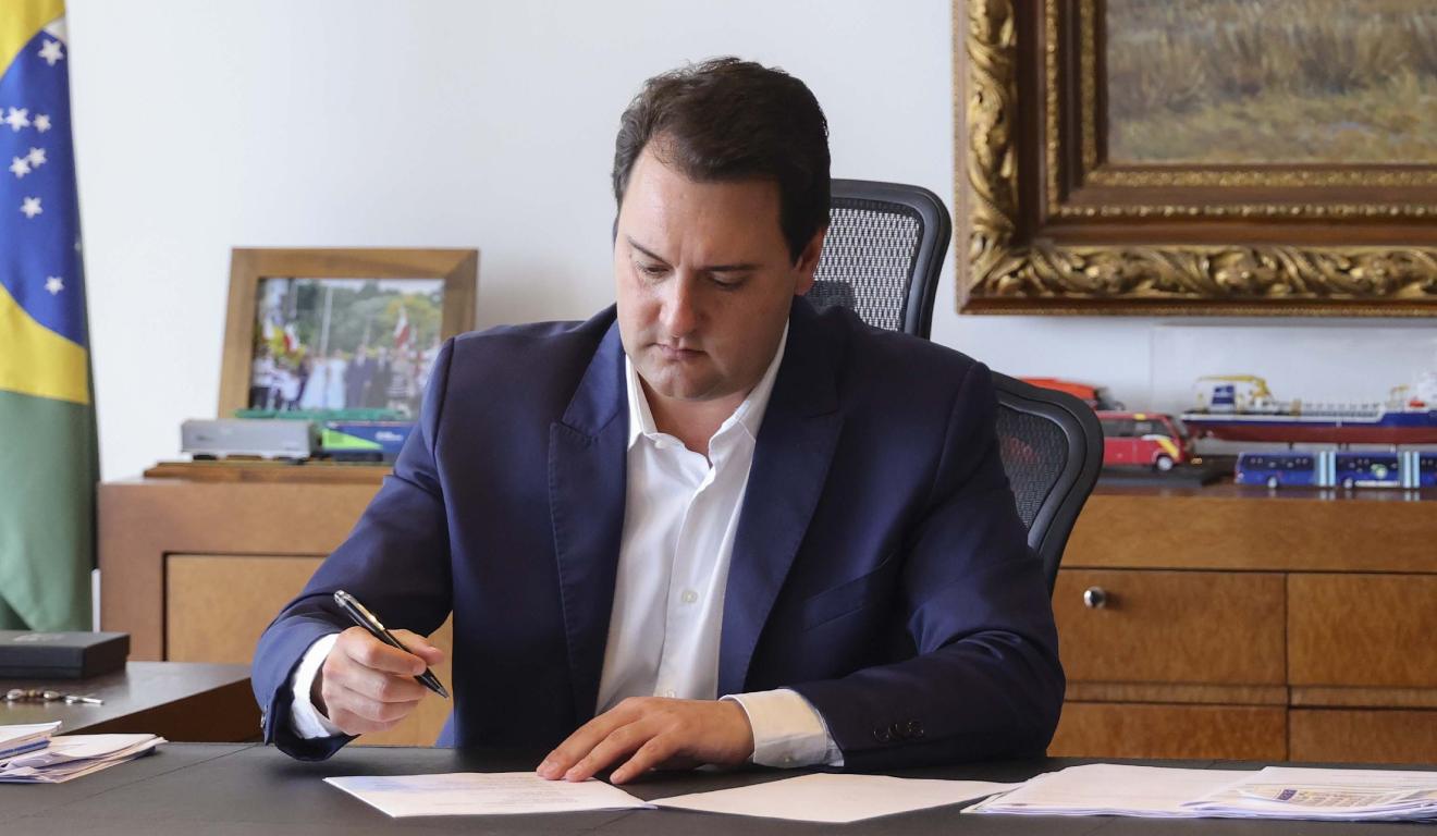 Ratinho Junior sentado na cadeira assinando folha